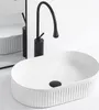 A white oval countertop sink with a black faucet, shown in a clean, minimalist bathroom setting. Náhled obrázku produktu