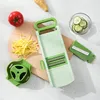 A kitchen mandoline slicer set with various attachments and ingredients like ginger, tomato, and cucumber. Produktbild-Vorschau