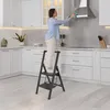 A woman is cleaning a kitchen range hood while standing on a step stool. Náhled obrázku produktu