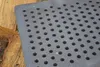 A close-up of a metal grate with circular holes, placed on top of a pile of wood. Náhled obrázku produktu