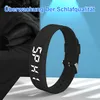 A black digital watch with a white display is shown in the foreground, with a blurred image of a person sleeping in bed in the background. Produktbild-Vorschau