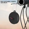 A small, round Bluetooth speaker is attached to a bicycle handlebar with a carabiner clip. Produktbild-Vorschau