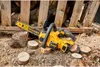 A yellow and black DeWalt battery-powered chainsaw rests on several small wood rounds, surrounded by sawdust and larger logs, with a wooden structure in the background. Voir les images du produit