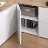 A close-up view of a white corner cabinet with a wood-tone countertop, showing an open door revealing shelves with books and a storage box. Náhled obrázku produktu