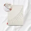 A fitted sheet is shown folded on a white surface, with a close-up inset showing hands tucking the sheet onto a mattress. Produktbild-Vorschau