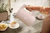 A person is pouring hot water from a pink electric kettle into a teacup on a kitchen counter. Produktbild-Vorschau