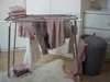 A drying rack with clothes is set up in a room with a dresser and a storage ottoman. Produktbild-Vorschau
