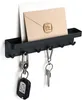 A black key holder with a shelf for mail is mounted on a white wall. Two sets of keys are hanging from the hooks. Produktbild-Vorschau