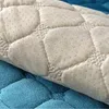 Nahaufnahme einer beigen gesteppten Matte mit Anti-Rutsch-Noppen auf einer Seite, teilweise über eine blaue strukturierte Oberfläche gefaltet Náhľad obrázku produktu