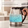 A hand holding a glass electric kettle filled with boiling blue water, with steam rising. Produktbild-Vorschau