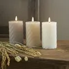 Three LED candles with a swirling texture are placed on a wooden surface, with dried wheat stalks in the foreground. Produktbild-Vorschau