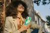 A woman is sitting outdoors, holding a smartphone. Náhled obrázku produktu