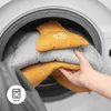 A hand is placing a yellow baby bouncer into a washing machine. Produktbild-Vorschau