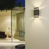An outdoor wall light illuminates a modern patio area with a sofa and a plant visible through a glass door. Anteprima dell’immagine prodotto
