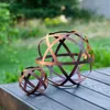 Two metal garden spheres with a rustic, rusted finish are placed on a wooden table outdoors, with a blurred green garden in the background. Voir les images du produit