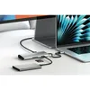 A Satechi USB-C Multiport Adapter is connected to a laptop, with an external hard drive and an SD card also connected to the adapter. A second monitor is visible in the background. Produktbild-Vorschau