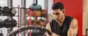 A man is working out in a gym with battle ropes and wearing black in-ear headphones. Produktbild-Vorschau