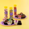 Three bottles of sprinkles and decorated brownies on purple plates against a yellow background. Produktbild-Vorschau