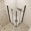 A corner shower enclosure with a black frame and frosted glass panels, set against a tiled wall and speckled floor. Produktbild-Vorschau