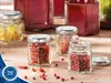 Several small hexagonal glass jars filled with various spices and preserved fruits are arranged on a wooden surface. Voir les images du produit