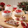 A collection of Christmas-themed ceramic serving dishes and bowls arranged on a wooden table, with a Christmas tree and poinsettia in the background. Anteprima dell’immagine prodotto
