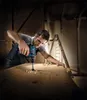 A man is using a cordless drill to drill a hole in a wooden surface in what appears to be a workshop or construction site. Voir les images du produit