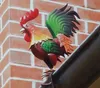 A colorful metal rooster figurine is perched on a dark gutter against a brick wall. Produktbild-Vorschau