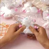 Hands holding a white cat-like toy in a clear plastic bag, surrounded by similar toys in bags. Voir les images du produit