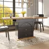 A dining table with an extendable top and storage drawers, set in a modern dining room with a large window overlooking autumn trees.