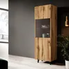 A tall, narrow wooden display cabinet with a glass section is shown in a modern living room setting. Náhled obrázku produktu