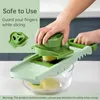 A person is using a green mandoline slicer to slice a potato into a glass bowl. Produktbild-Vorschau