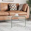 A glass coffee table is placed in front of a brown leather couch, with a cup of coffee and a glass of water on it. Anteprima dell’immagine prodotto