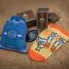 A collection of One Piece themed merchandise, including a drawstring bag, socks, and decorative treasure chests, arranged on a sandy surface. Produktbild-Vorschau