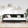 A black velvet corner bed frame with a white mattress and pillows, set against a white wall with two shelves decorated with books and ornaments. A floor lamp and a potted plant are also visible. Podgląd zdjęcia produktu