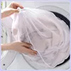 A person is putting a white mesh laundry bag filled with clothes into a washing machine. Produktbild-Vorschau