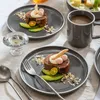 A table setting with two plates of dessert, a mug of coffee, and a candle holder. Produktbild-Vorschau