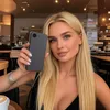 A woman is holding up a phone case in a cafe setting. Produktbild-Vorschau