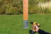 A wooden post is being secured to the ground with a metal bracket and a power drill. Produktbild-Vorschau
