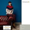 A woman is sitting on a leather couch wearing a sweater and plaid pants. Produktbild-Vorschau