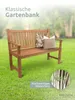 A wooden garden bench with two pillows on it, placed on a green lawn with trees in the background. There is text overlay and a circular inset image showing tree trunks. Produktbild-Vorschau