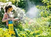 A woman is spraying plants in a garden with a pressure sprayer. Produktbild-Vorschau