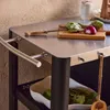 A close-up view of a stainless steel outdoor serving cart with a cutting board, artichokes, and red onion on top. A wooden spoon hangs from a hook. Produktbild-Vorschau