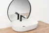 A white oval countertop sink with a black faucet is shown in front of a round mirror. Náhled obrázku produktu