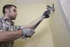 A man is using a pry bar to remove material from a wall. Podgląd zdjęcia produktu