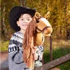 A young boy wearing a cowboy hat and a patterned sweater is holding a stick horse in an outdoor setting with trees in the background. Anteprima dell’immagine prodotto