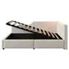 A beige upholstered bed frame with the mattress support lifted to reveal storage space underneath. The bed has a headboard with subtle lighting. Voir les images du produit