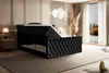 A bedroom scene with a black velvet upholstered bed with its storage compartment open, showcasing the mattress and topper. The room has a modern, luxurious feel with soft lighting and decorative elements. Produktbild-Vorschau