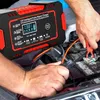 A person is using a car battery charger to charge a car battery. Podgląd zdjęcia produktu