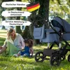 A woman and child are sitting on the grass next to a blue stroller in a park. Produktbild-Vorschau