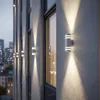 Exterior wall lights illuminate a building facade at dusk, with a city skyline in the background. Podgląd zdjęcia produktu